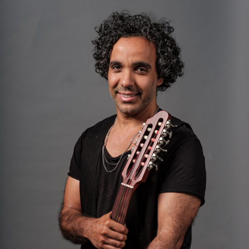 Mohamed Ahaddaf is ud-speler bij Marmoucha Orchestra. Mohamed is componist, musicus en gespecialiseerd in Midden-Oosterse en Noord-Afrikaanse muziek. Mohamed staat op deze foto voor een grijze muur met een ud in zijn handen.