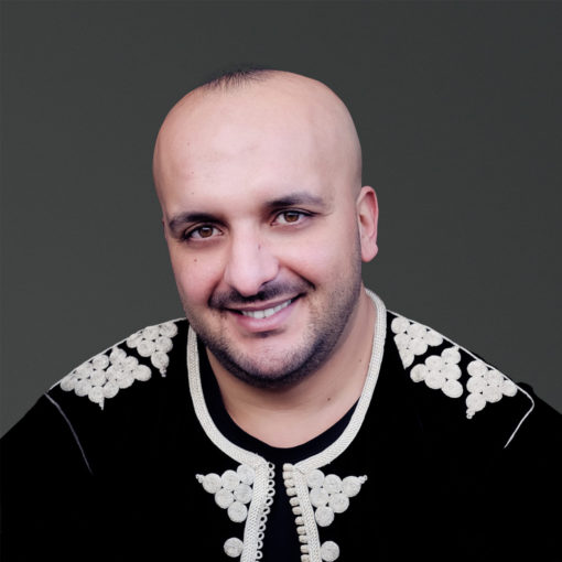 Adil Chaoui is zanger bij Marmoucha Orchestra en gespecialiseerd in Andalusische muziek. Adil staat op deze foto voor een grijze muur.