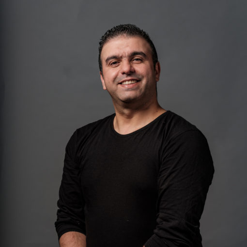 Emad Ghajjou is Percussionist bij Marmoucha Orchestra. Emad staat op deze foto voor een grijze muur.