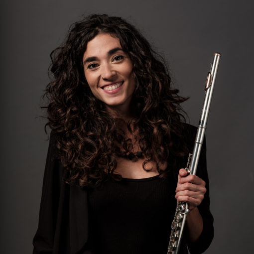 María Cristina González is fluitist bij Marmoucha Orchestra en gespecialiseerd in klassieke muziek en oude muziek. Maria staat op deze foto voor een grijze muur met een dwarsfluit in haar handen.