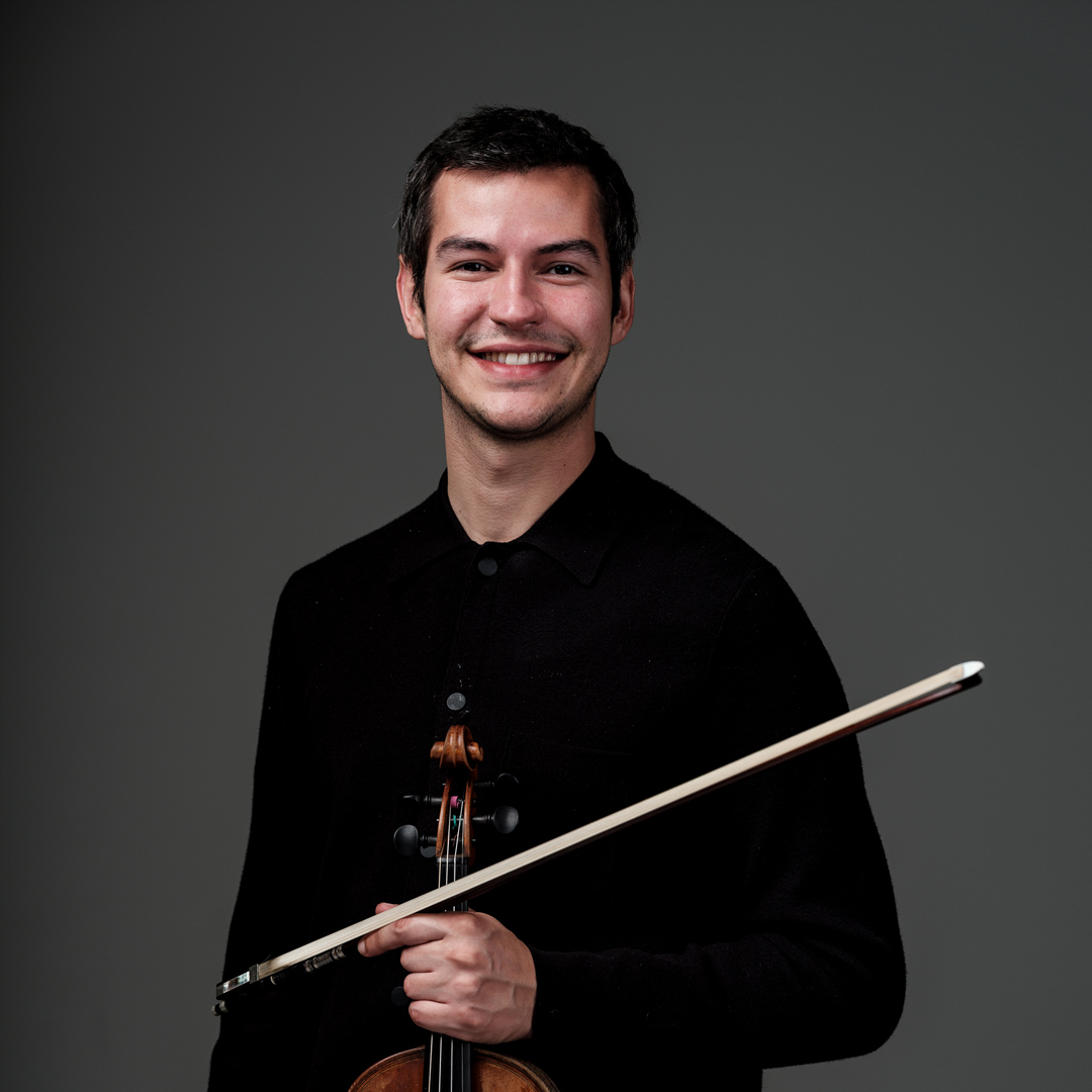 André Felipe Lima is violist bij Marmoucha Orchestra. André staat op deze foto voor een grijze Muur met een viool in zijn handen.