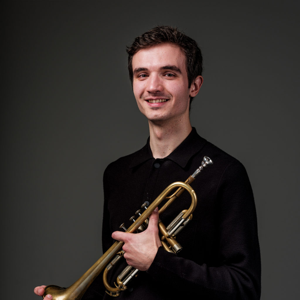 Antonio Moreno Glazkov is trompettist bij Marmoucha Orchestra. Antonio staat op deze foto voor een grijze muur met een trompet in zijn handen.
