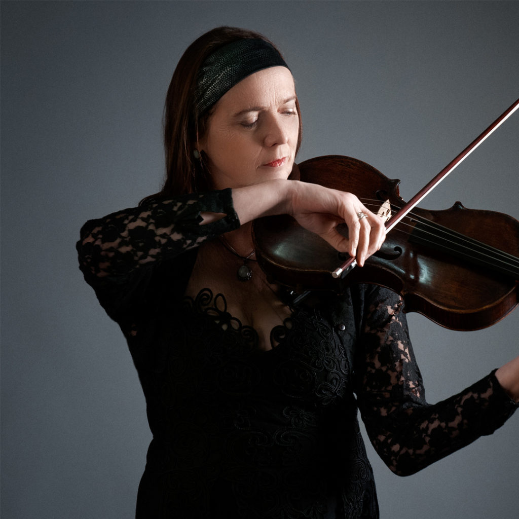 Irma Haverkamp is altvioliste bij Marmoucha Orchestra. Irma staat op de foto voor een grijze muur, spelend op de viool.