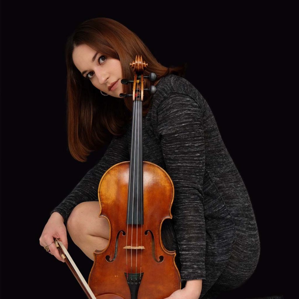 Kardelen Buruk is altvioliste bij Marmoucha Orchestra. Kardelen zit op deze foto, voor een zwarte achtergrond, op haar hurken met een altviool.