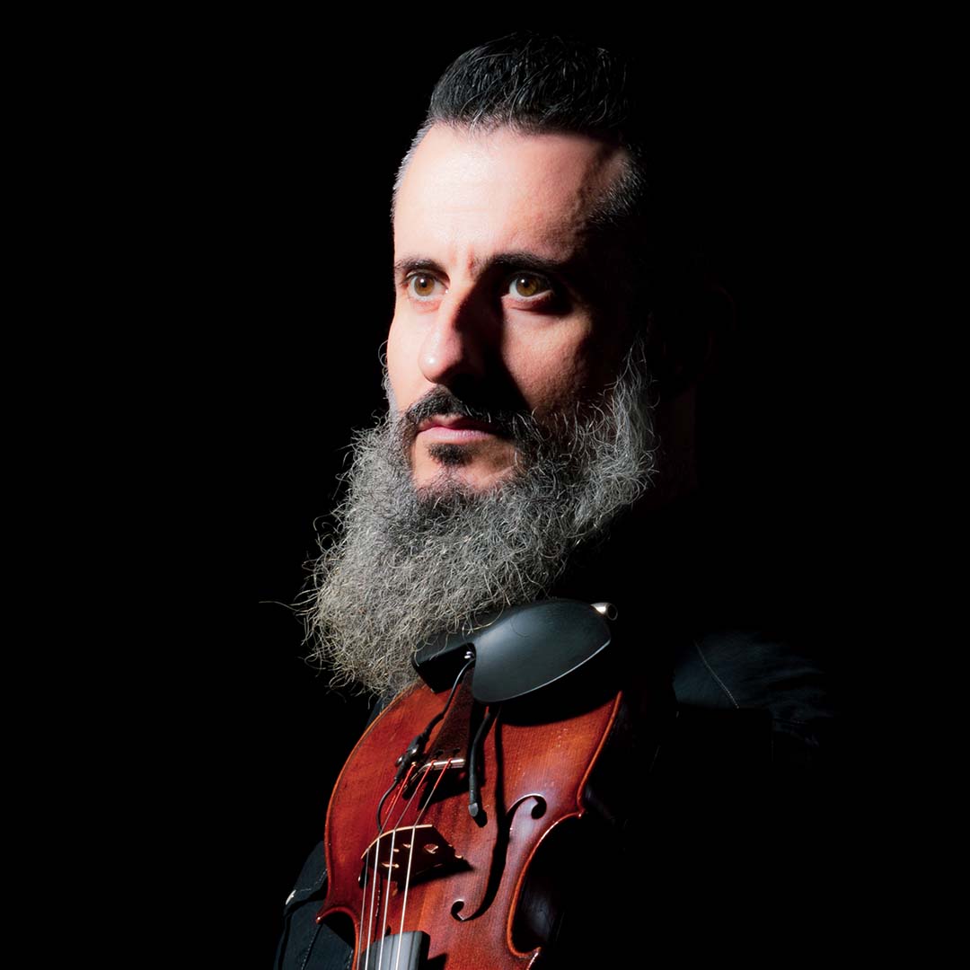 Luis Mascaro is violist bij Marmoucha Orchestra. Luis staat op deze foto voor een zwarte achtergrond en heeft een viool bij zich.