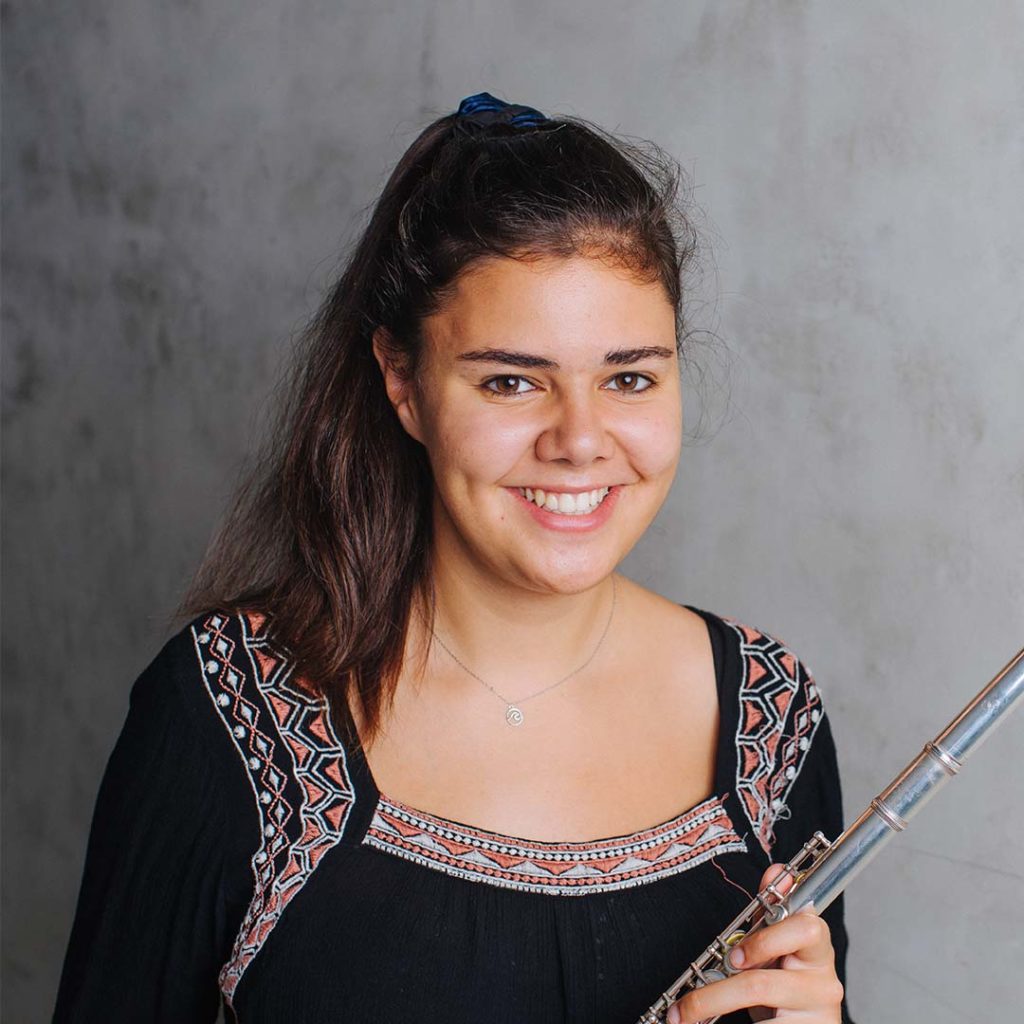 Marta Gonçalves Vilaça is fluitiste bij Marmoucha Orchestra. Marta staat op deze foto voor een grijze muur met een dwarsfluit in haar handen.