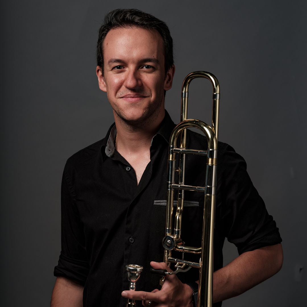 Pablo Martínez is trombonist bij Marmoucha Orchestra. Pablo staat voor een grijze muur met een trombone in zijn handen.