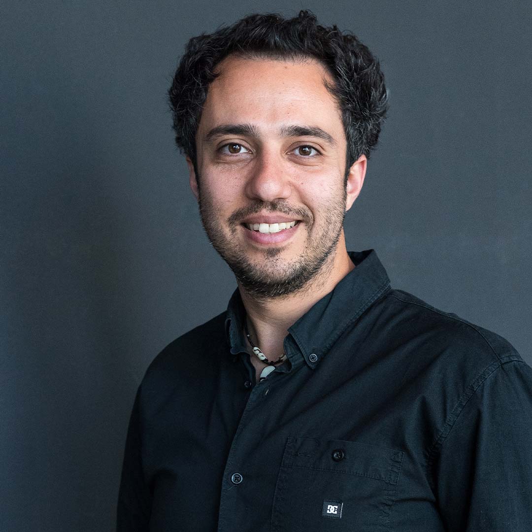 Shayan Fathi is veelzijdig muzikant bij Marmoucha Orchestra. Hij staat op deze foto voor een grijze muur.